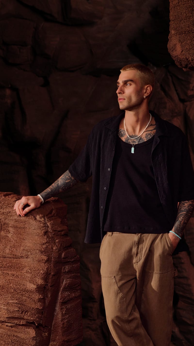 Model wearing a turquoise beaded bracelet and pendant poses in a rocky, desert scene.